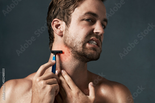 Razor, shaving or man in studio with pain or hair removal for skincare tools, face grooming or cosmetics. Uncomfortable, rough irritation and model on grey background for neck shaver and wellness photo