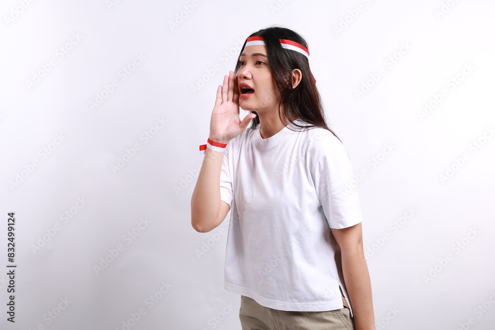 Young Asian woman wearing red white flag ribbon shouting loud at copy space, telling about good sale offer isolated over white background. Celebrate Indonesian independence day on 17 August Young Asian woman wearing red white flag ribbon shouting loud at copy space, telling about good sale offer isolated over white background. Celebrate Indonesian independence day on 17 August