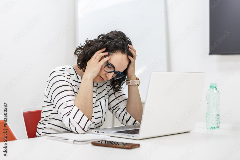 Stressed Woman Holding Head in Office While Working on Laptop Stressed Woman Holding Head in Office While Working on Laptop