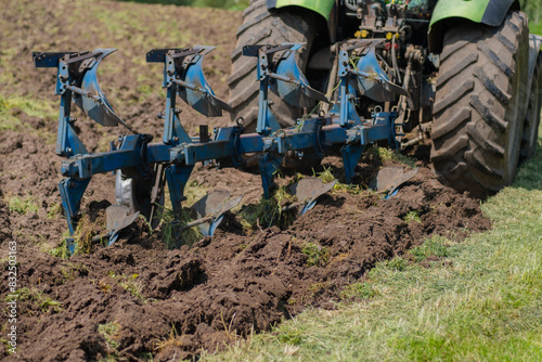 A tractor plows a field in early spring. A blue plow breaks the ground for sowing agricultural crops. Cultivation of virgin soil, sowing campaign in rural areas