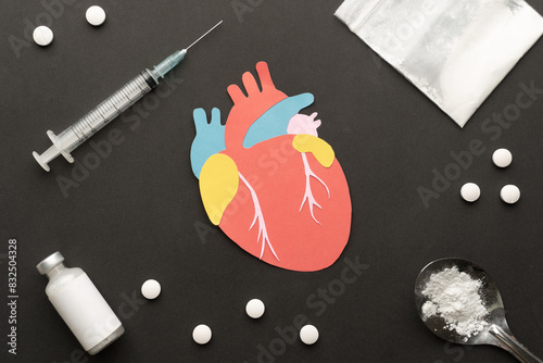 Effects of drugs on the human heart. Paper cut of heart with drug powder, syringe and pills on dark background. International Day against Drug Abuse.
