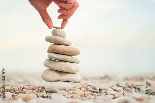 A person is holding a rock on top of a stack of rocks. Concept of balance and stability, as the person is carefully placing the rock on top of the others