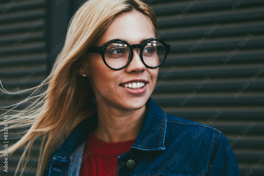 Positive young woman with blonde hair laughing while looking away outdoors.Hipster girl in optical spectacles dressed in stylish denim apparel standing on black promotional background Positive young woman with blonde hair laughing while looking away outdoors.Hipster girl in optical spectacles dressed in stylish denim apparel standing on black promotional background
