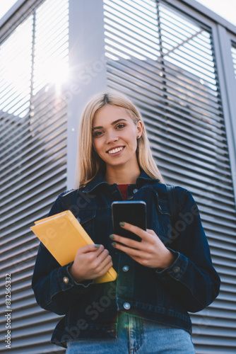 Foto Half length portrait of pretty smiling blonde blogger sending funny messages to friends via modern smartphone