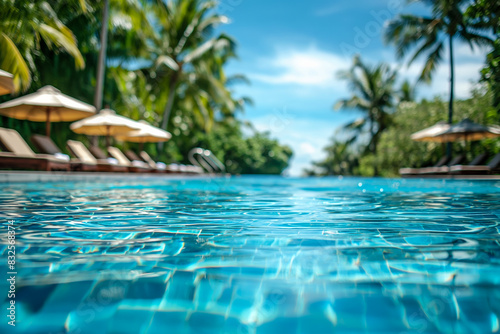 Closeup of a tropical pool, clear turquoise water, sun loungers, palm trees in the background  © fotogurmespb