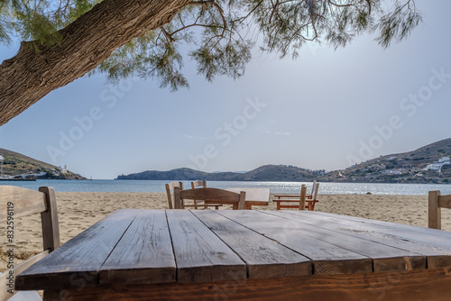 View of tables and chairs next to a tree at the Gialos Beach in Ios Greece photo