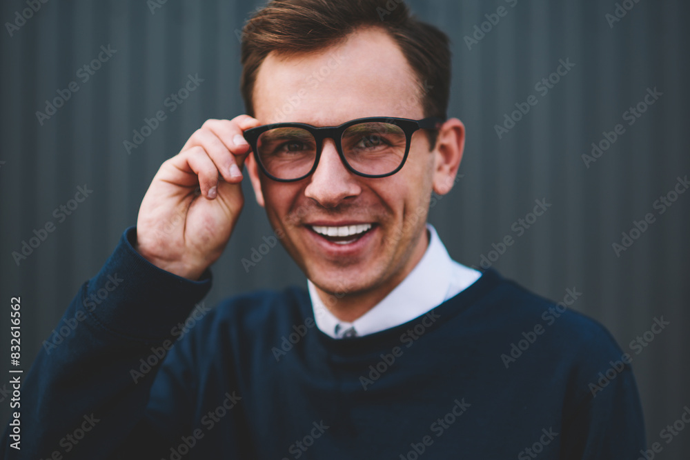 Half length portrait of handsome cheerful male person in trendy eyeglasses spending free time at summer street.Close up image of young happy hipster guy looking at camera while correcting spectacles