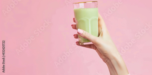 Woman hand with pink nails holding green smoothie glass isolated on pastel background photo