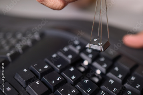 In a closeup shot, a hand is seen using a keycap puller tool to meticulously remove a keyboard key photo