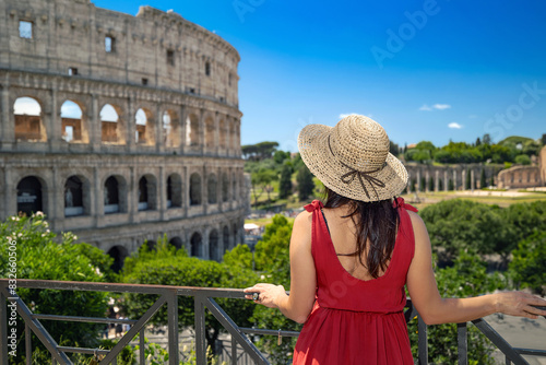 Photos Brunette girl with straw hat admires the majesty of the Colosseum and in the background the ancient ruins of the Roman Forum in Rome, Italy