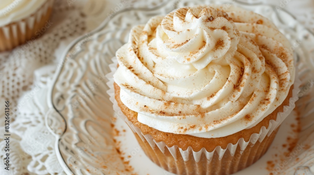 A cupcake, topped with white frosting and cinnamon sprinkles, rests atop a glass plate Nearby, a second cupcake resides on A cupcake, topped with white frosting and cinnamon sprinkles, rests atop a glass plate Nearby, a second cupcake resides on