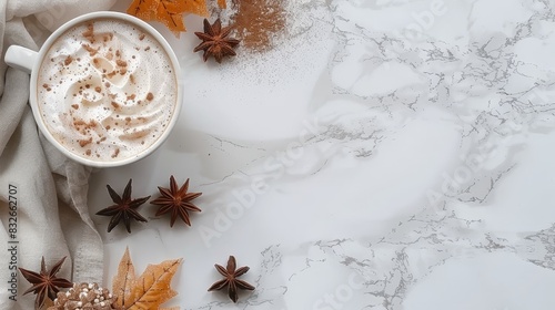  An overhead view of a steaming hot chocolate cup on a white marble table Autumn leaves surround it  and star anisettes rest atop the drink and among the leaves