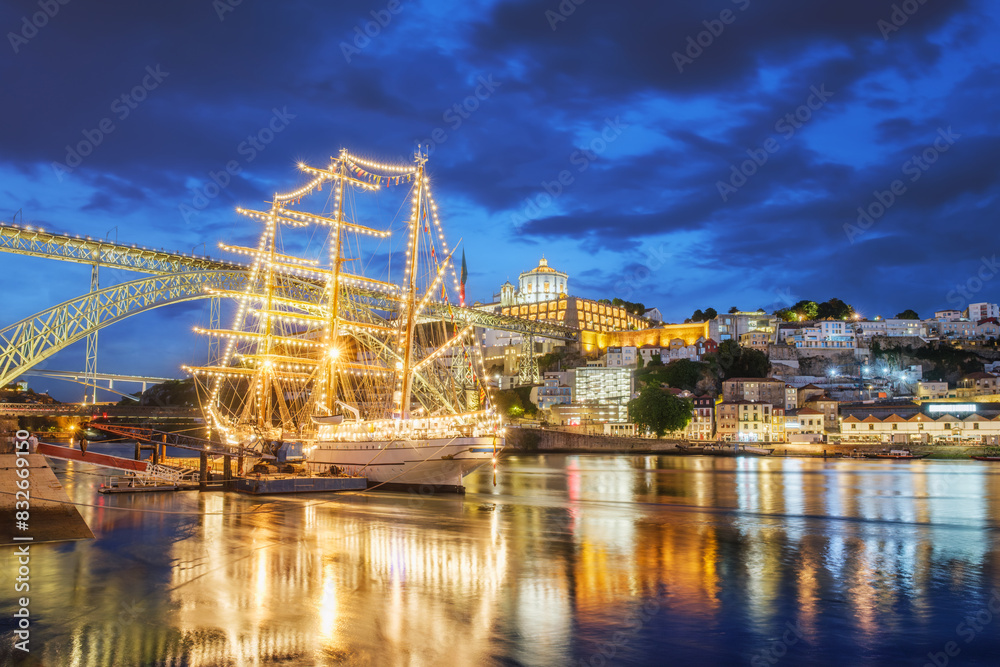 Fototapeta premium View of Vila Nova de Gaia city with a sailing ship and Dom Luis I bridge over Douro river in the evening. Porto, Portugal