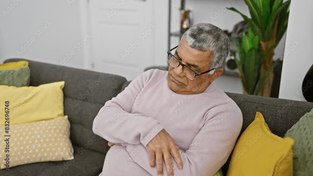 Mature grey-haired man relaxing on sofa indoors, reflecting contentment and comfort in a living room setting with colorful pillows. Mature grey-haired man relaxing on sofa indoors, reflecting contentment and comfort in a living room setting with colorful pillows.
