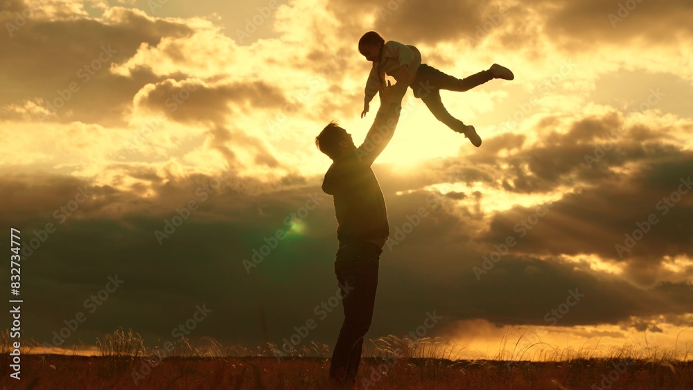 Concept, family safety trust, Dad plays with his daughter, throws child into sky with his hands, happy kid. Silhouette, Father of daughters playing together in park against backdrop of sun and clouds