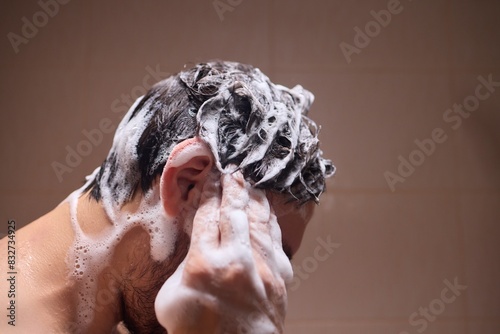 Fotografía Man washing hair with shampoo in shower, creating foamy lather - personal hygiene care