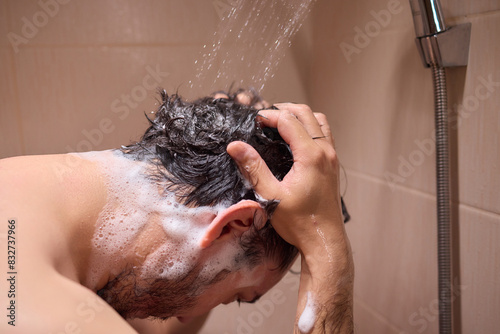 Man washing hair with shampoo in shower, creating foamy lather - personal hygiene care.