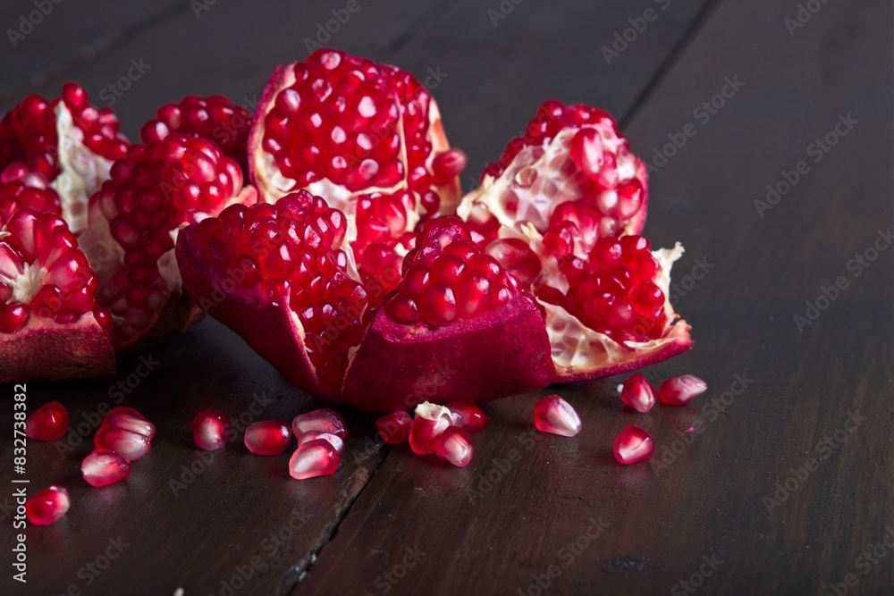 Close-up of ripe, fresh pomegranate cut open with view of seeds on a wooden table Close-up of ripe, fresh pomegranate cut open with view of seeds on a wooden table