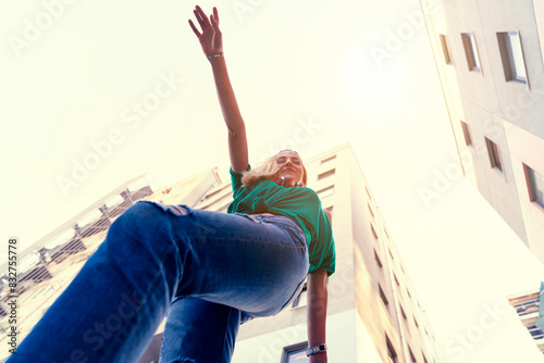 young cheerful woman dancing in the city and wearing headphones