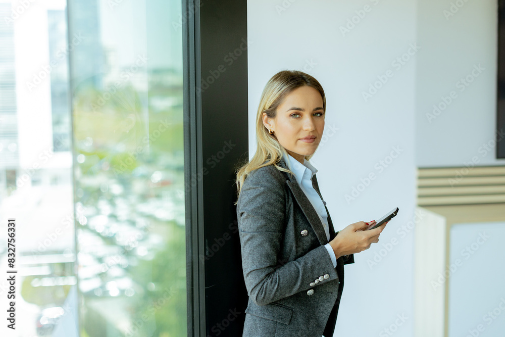 Fototapeta premium Young professional woman smiling with smartphone in modern office morning