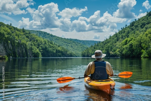 Senior Caucasian man kayaking on a clear lake with a backdrop of forested hills under a cloudy sky.