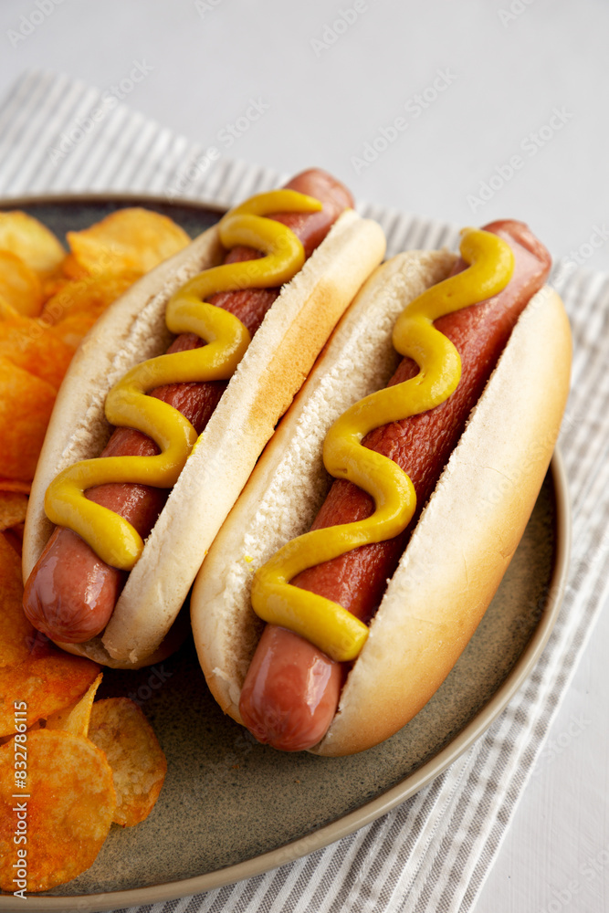 Homemade Hot Dog with Mustard and Potato Chips on a Plate, side view. Homemade Hot Dog with Mustard and Potato Chips on a Plate, side view.