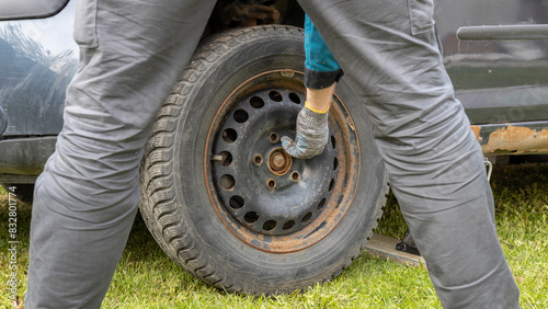 A man stands near a car and changes a winter tire on a spring day. Car parked on the grass, car repair at home.