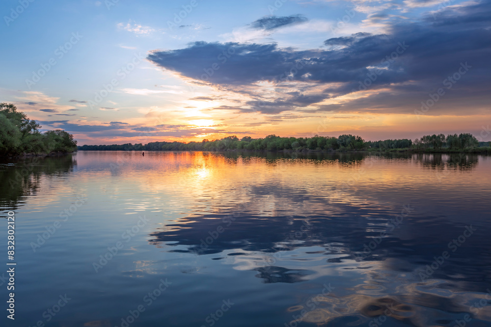 The sun, nestled among cotton candy clouds, dips below the horizon, casting gentle hues of orange and pink across the tranquil waters.