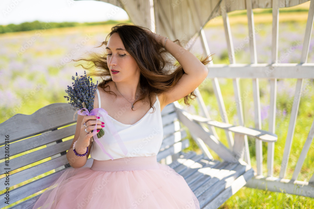 Fototapeta premium a beautiful girl in a dress with a bouquet of lavender flowers sits on a bench
