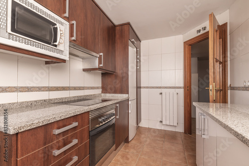 A kitchen with brown wooden cabinets, with integrated appliances, gray granite worktops and sapelly wood doors