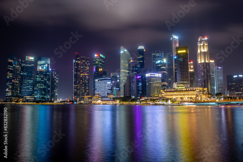 Panoramic night view of a vibrant city skyline reflected in the water with colorful lights