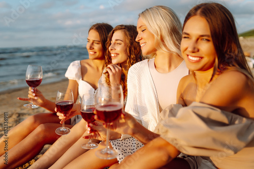 Happy young women drinking wine at summer day at the beach. Vacation, travel, sea, friendship and people concept. 