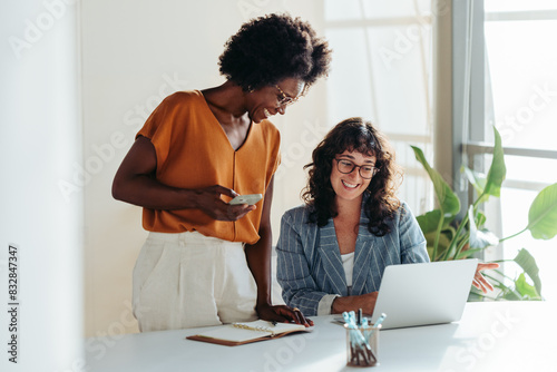 Two professional women collaborating happily over laptop in modern office