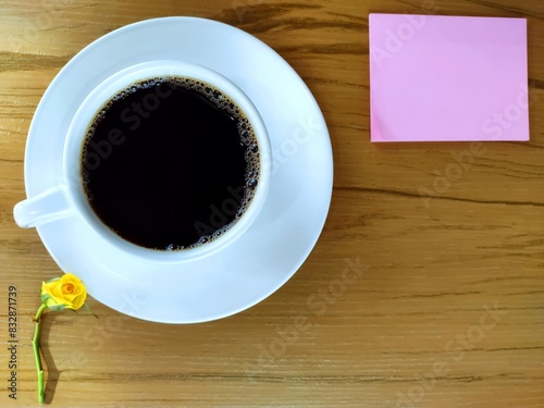 A cup of coffee  note pad and yellow rosebud on wooden table. Top view 