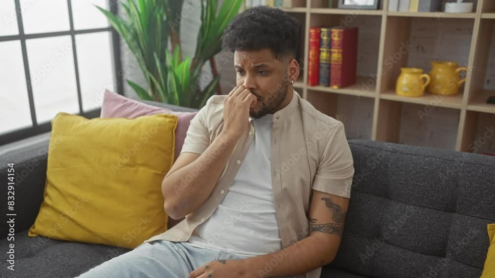 Stressed african american man, biting nails at home - anxiety problem pours out while nervously sitting on sofa, showing panic expression Stressed african american man, biting nails at home - anxiety problem pours out while nervously sitting on sofa, showing panic expression