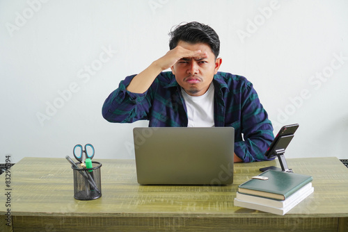 Billede på lærred young asian businessman sitting at workplace looking far away with hand to look