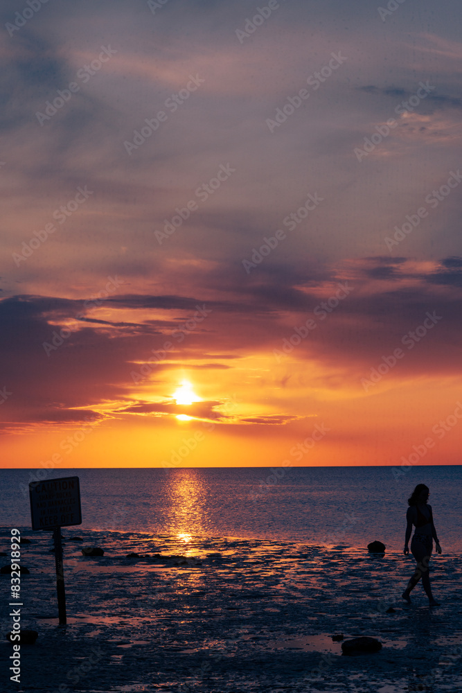 Silhouetted woman strolling on the beach at sunset near the sea