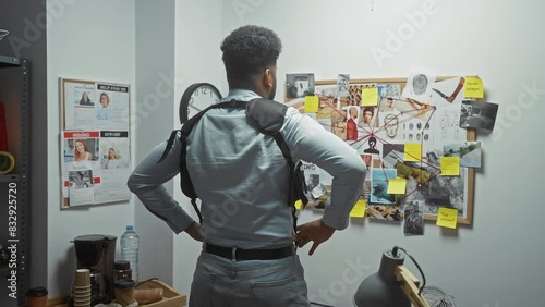 African american man wearing a shoulder bag stands before an evidence board in a detective's office. photo