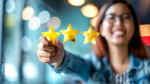 A smiling woman holding three yellow stars in her hand representing a high score, rating, reputation or positive feedback