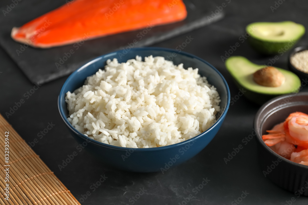 Cooked rice in bowl and other ingredients for sushi on dark table, closeup Cooked rice in bowl and other ingredients for sushi on dark table, closeup