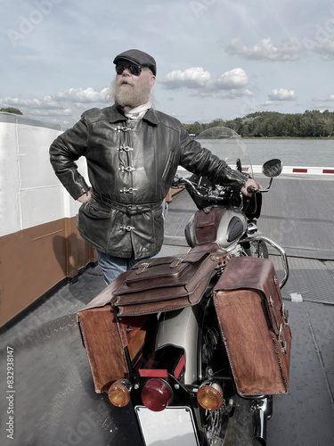 Mann mit langem Bart, steht mit seinem Retro Motorrad am Ufes des Rheins photo