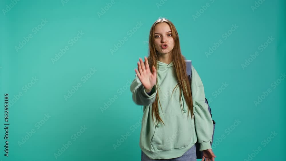 Assertive young woman doing stop hand gesture and talking. Annoyed girl doing firm halt sign gesturing, wishing to end concept, isolated over blue studio background, camera B