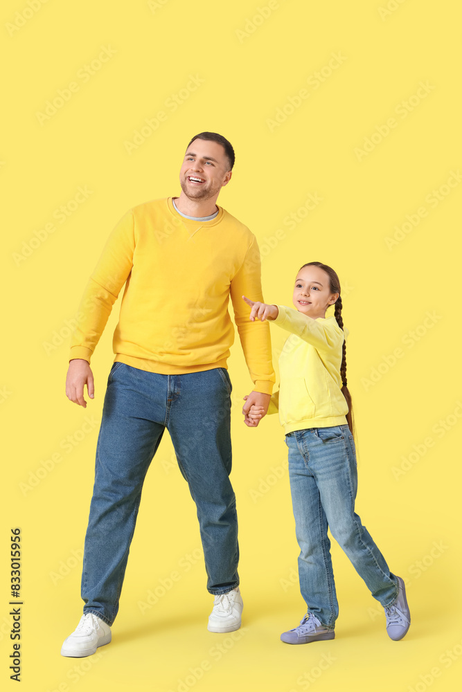 Little girl showing something to her father on yellow background Little girl showing something to her father on yellow background