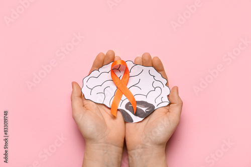 Schilderij op canvas Female hands with orange ribbon and paper brain on pink background