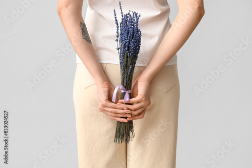 Beautiful young woman with bouquet of lavender flowers on light background