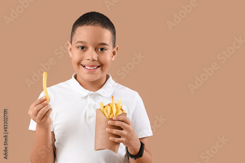 Happy little African-American boy with french fries on brown background