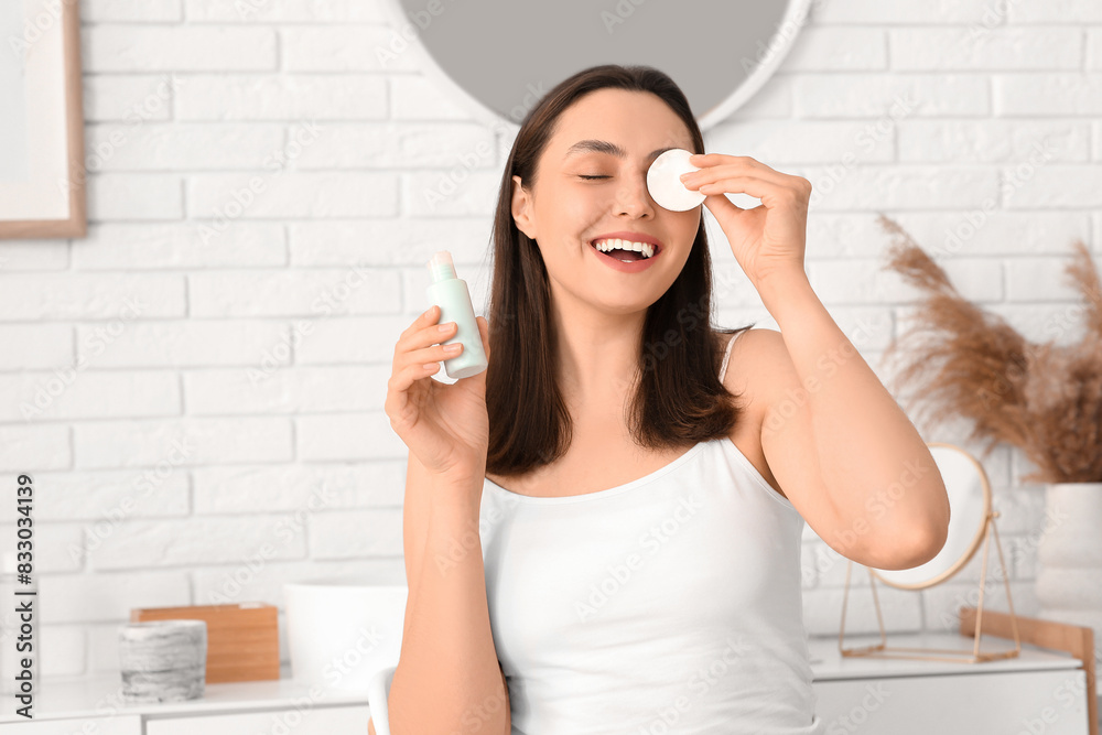 Happy young woman with cotton pad and micellar water for removing makeup in bathroom Happy young woman with cotton pad and micellar water for removing makeup in bathroom