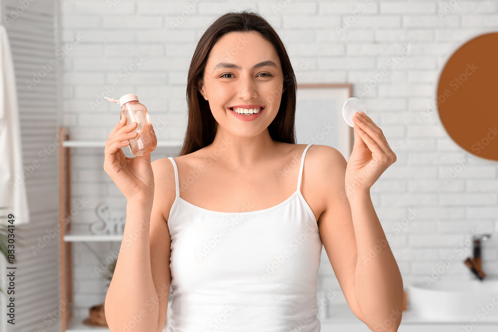 Happy young woman with cotton pad and micellar water for removing makeup at home Happy young woman with cotton pad and micellar water for removing makeup at home