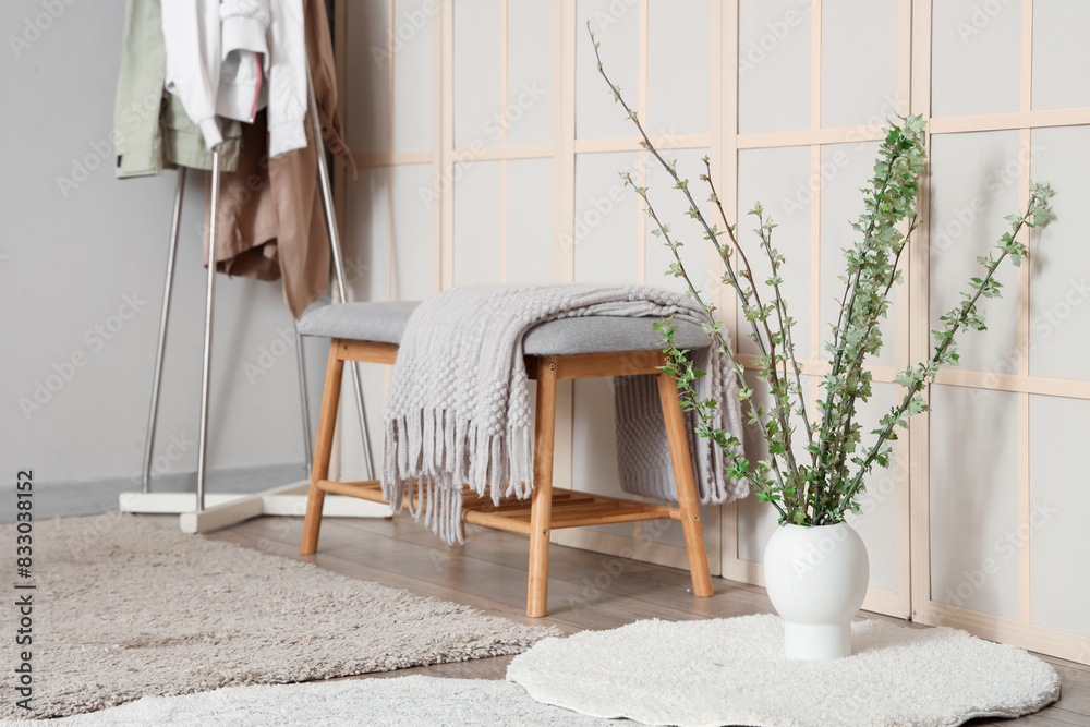 Soft bench, white rug and vase with blossoming branches in stylish room Soft bench, white rug and vase with blossoming branches in stylish room