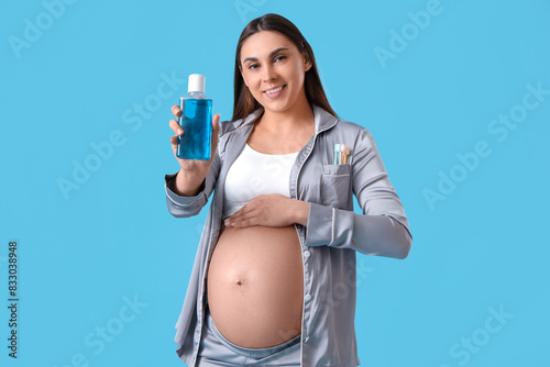 Young pregnant woman with mouth rinse on blue background